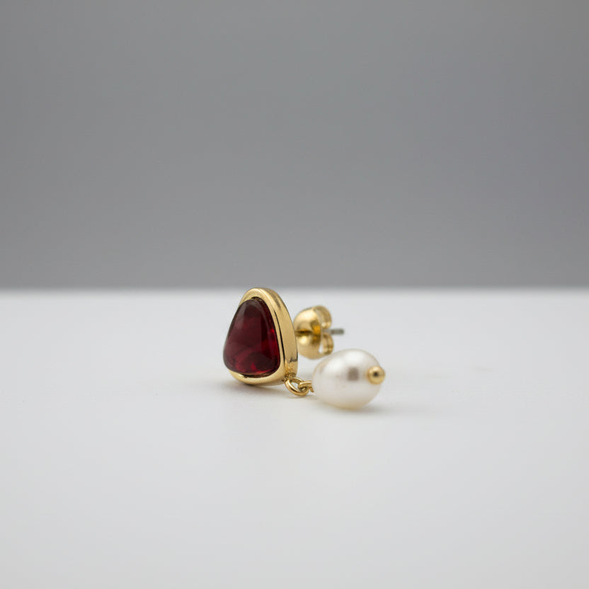 Gold earring with a red gemstone on a gray surface