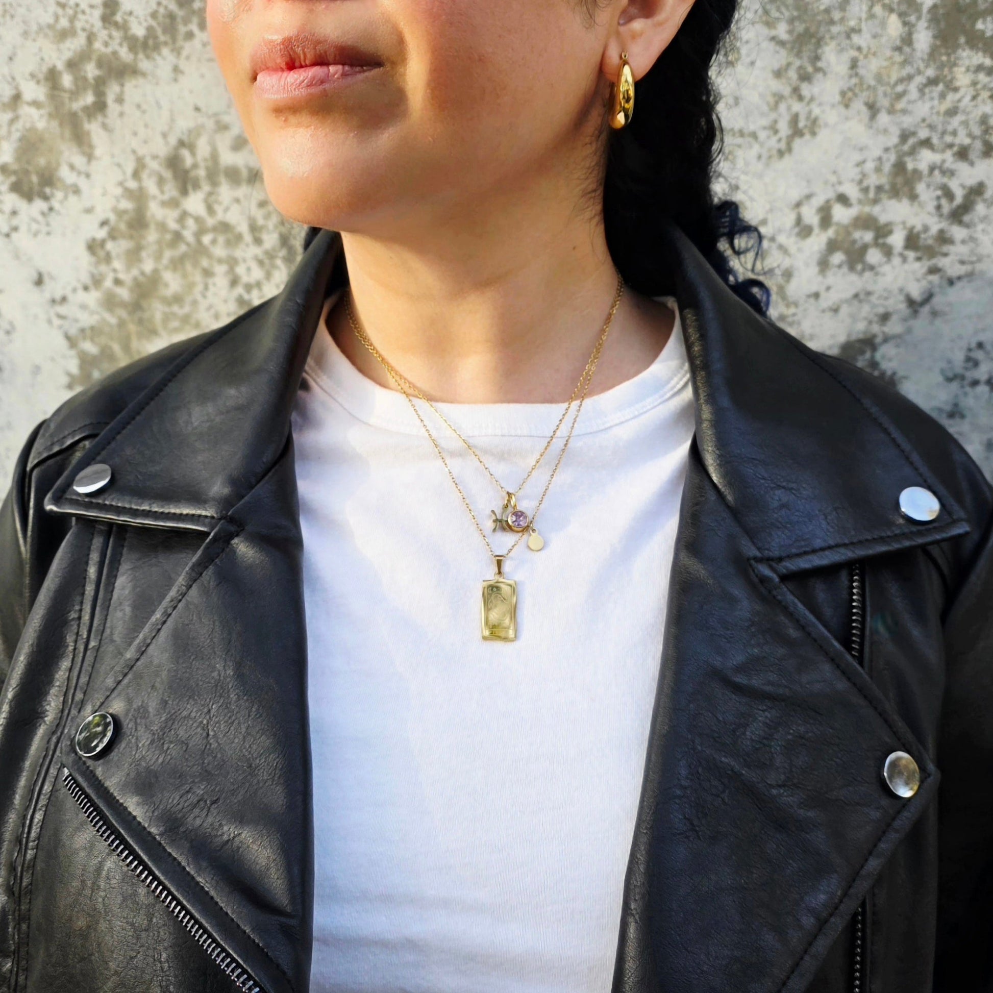 Person wearing a black leather jacket and white shirt against a textured wall.