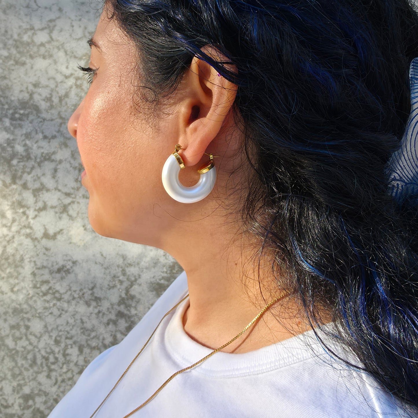 Pair of white hoop earrings with gold accents on a model on a light gray background.