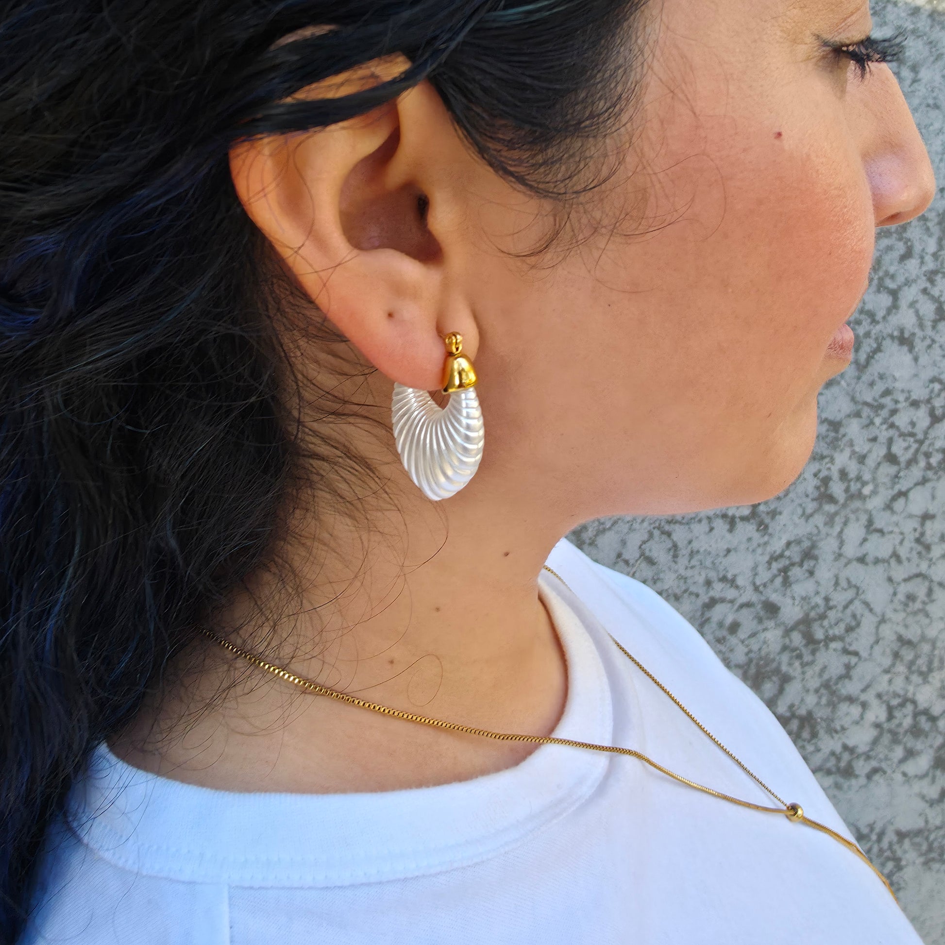 Pair of white hoop earrings with gold accents on a light gray background on a model.