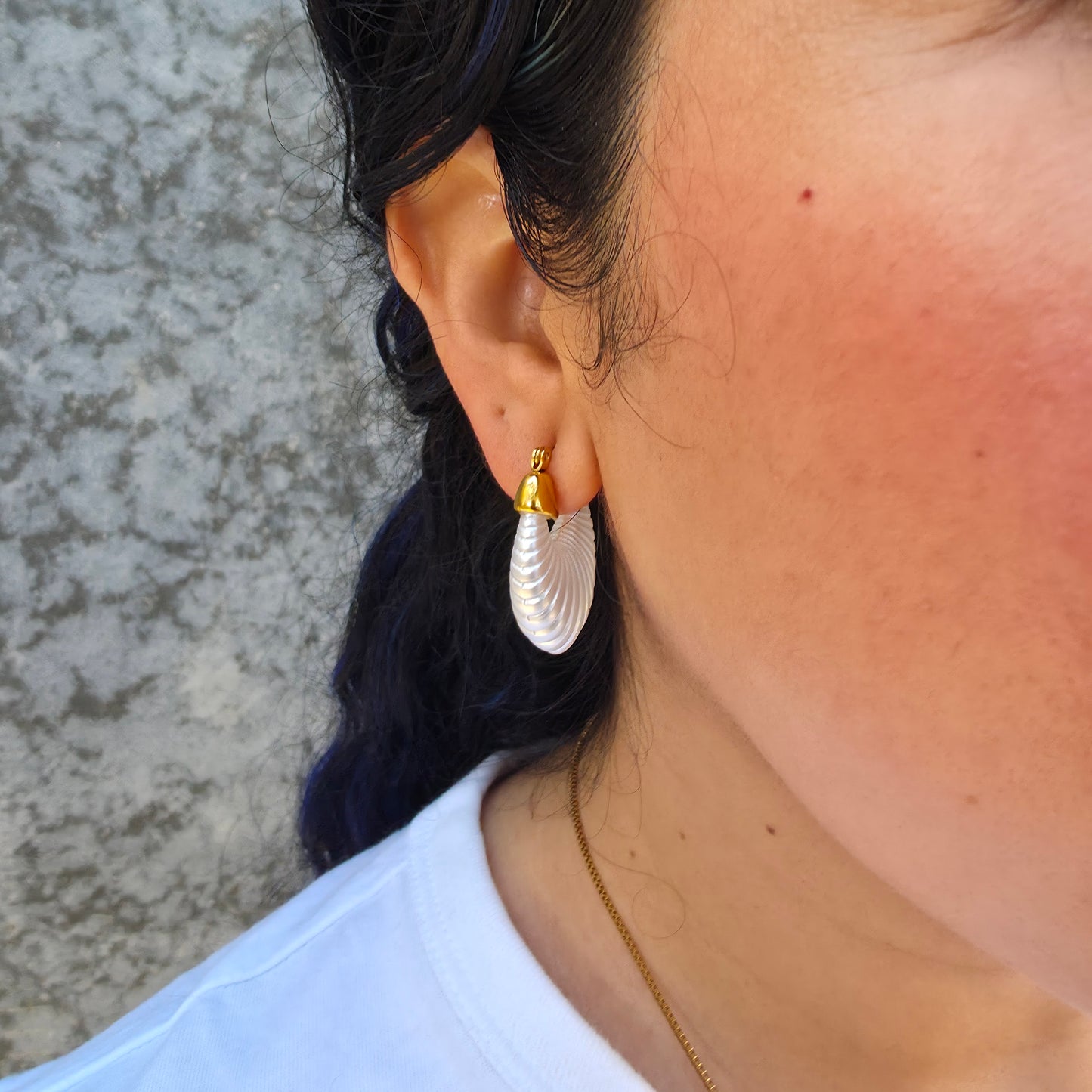 Pair of white hoop earrings with gold accents on a model on a light gray background
