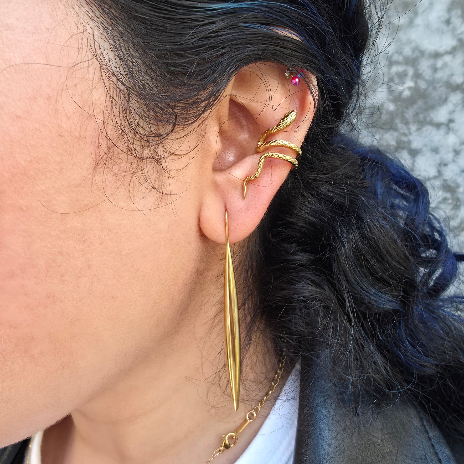 Close-up of an ear with gold earrings and a necklace, with hair partially covering the face.