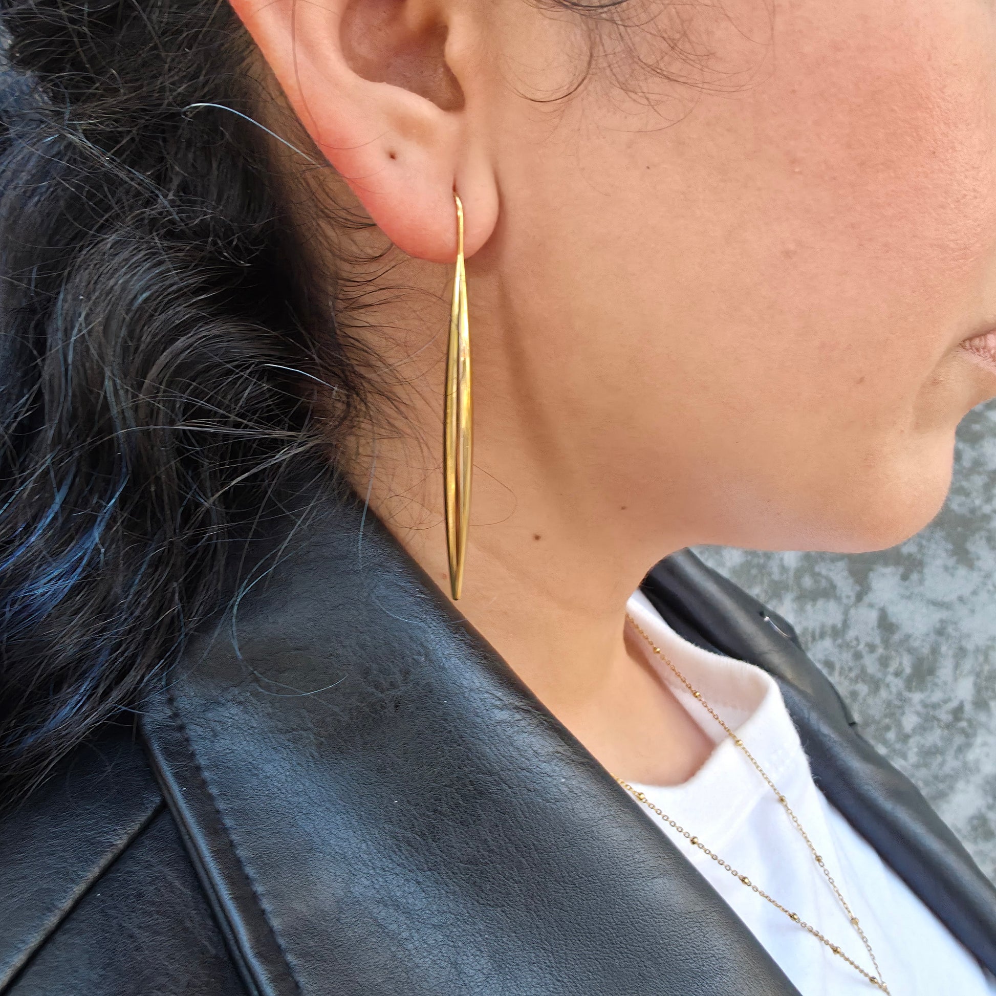 Close-up of a person wearing a gold earring with a blurred background
