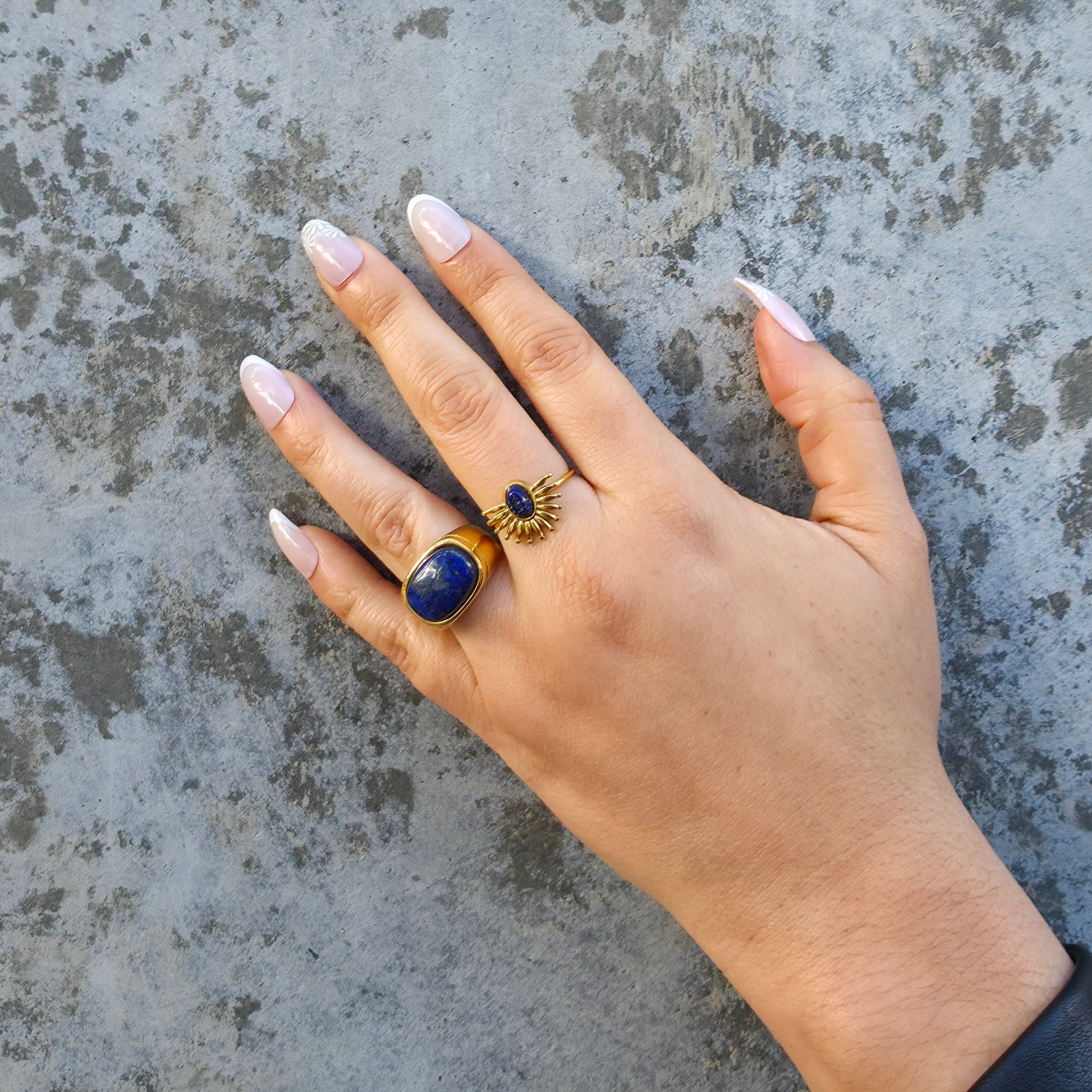 Hand wearing a gold and blue ring on a textured surface
