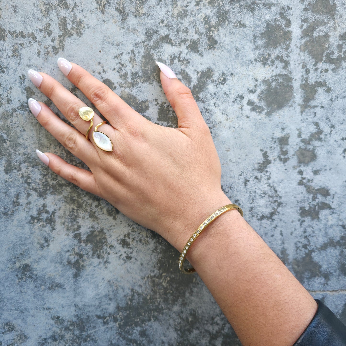 Hand wearing a gold ring and bracelet on a textured surface
