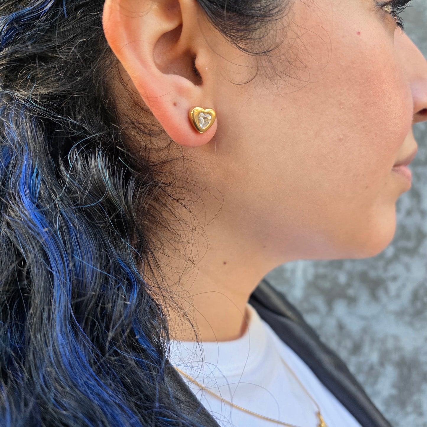 Close-up of an ear with a gold heart-shaped earring, hair with blue highlights.