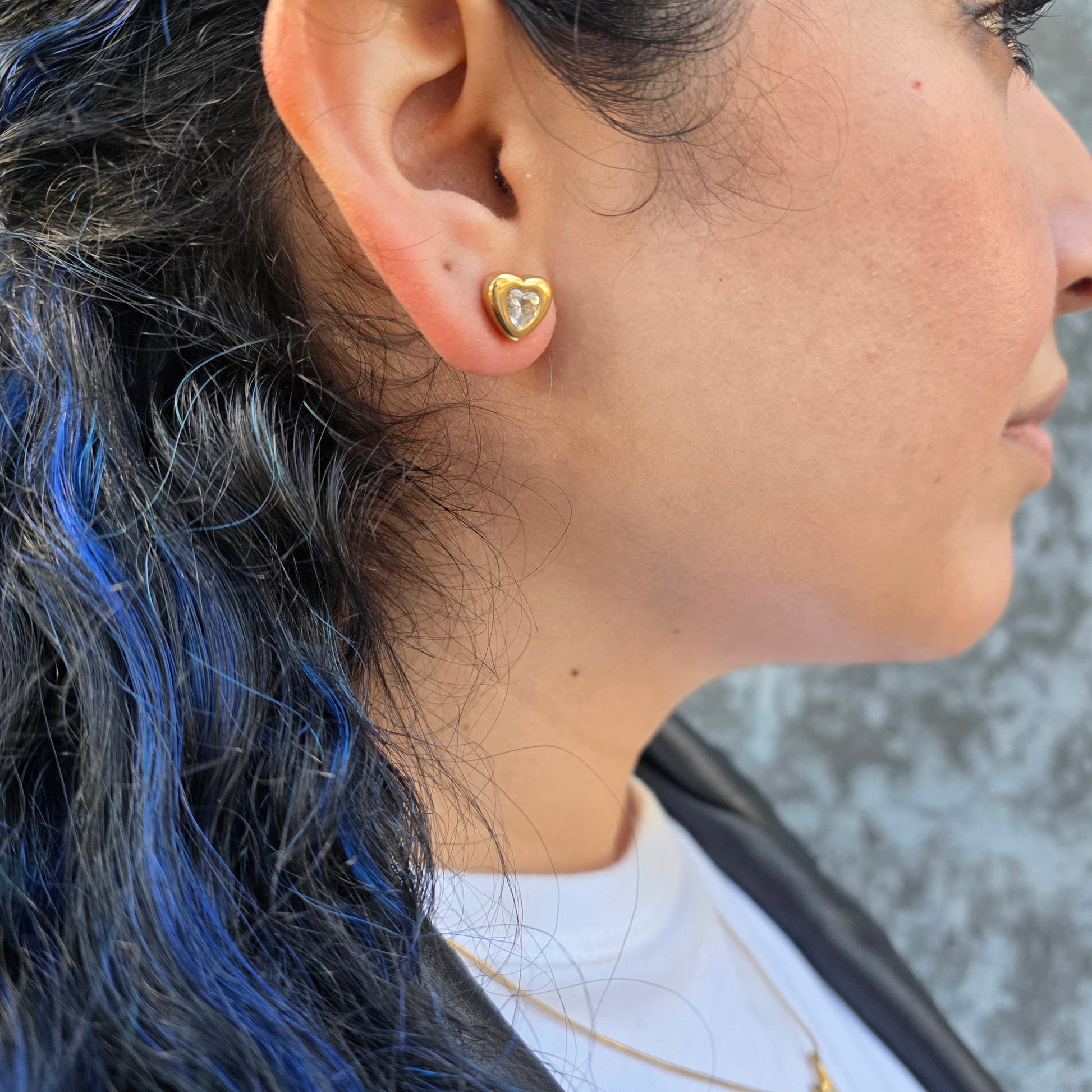 Close-up of an ear with a gold heart-shaped earring, hair with blue highlights.