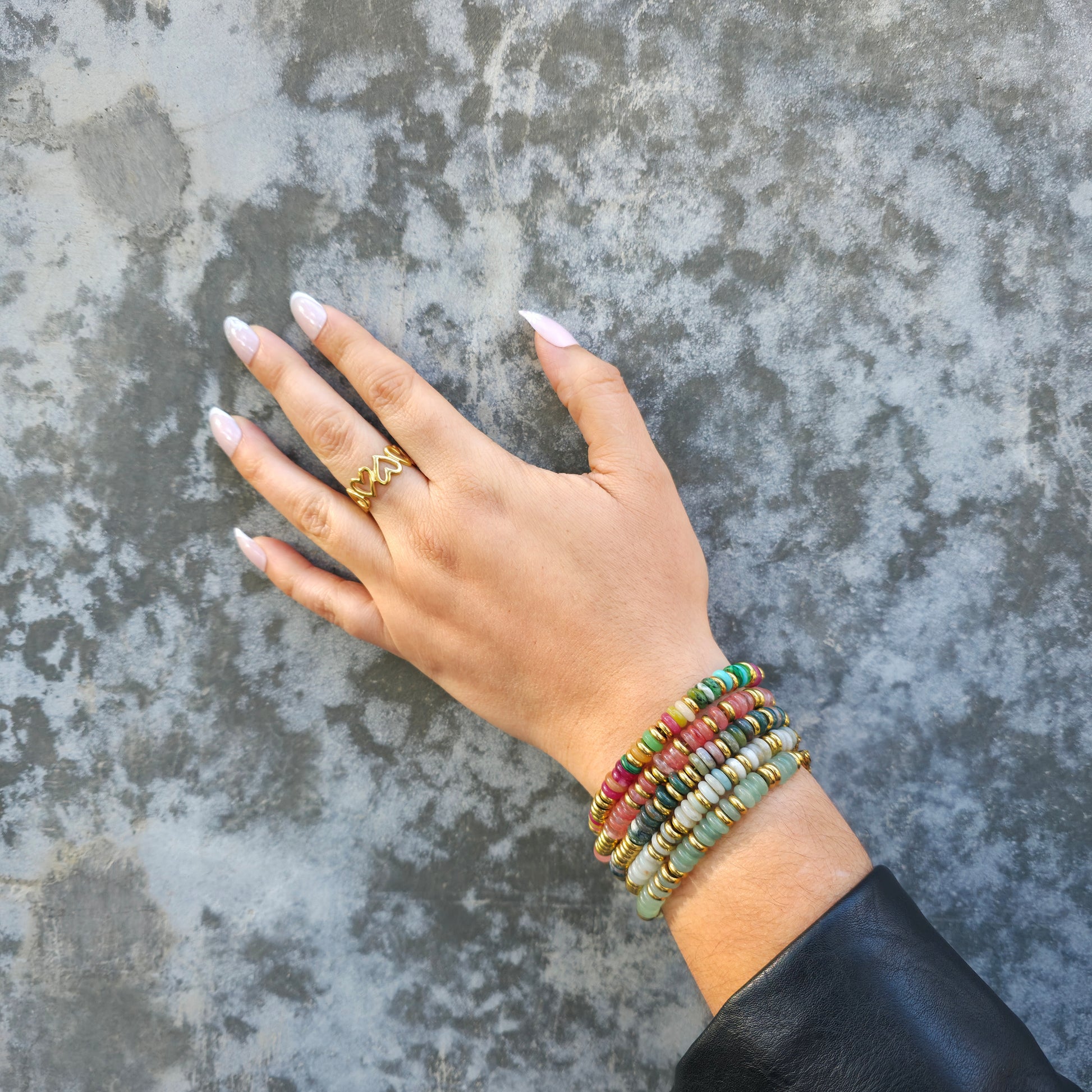 Hand wearing multiple beaded bracelets on a textured surface
