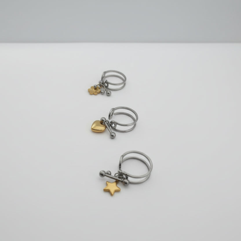 Three silver rings with gold charms on a light gray background