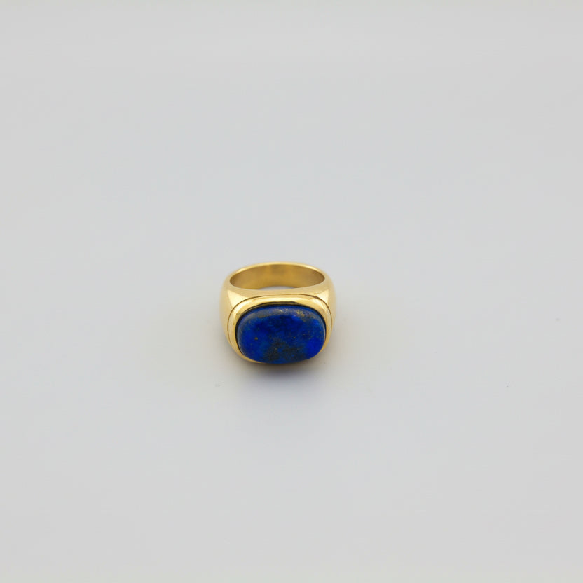 Gold ring with a blue stone on a light gray background