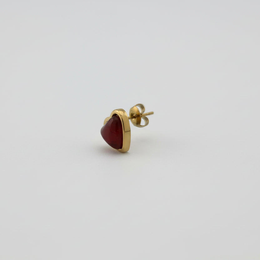Gold earring with a red gemstone on a white background