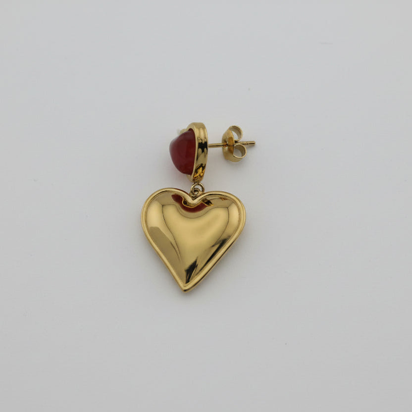Gold heart-shaped earring with red heart-shaped gemstone on a light gray background