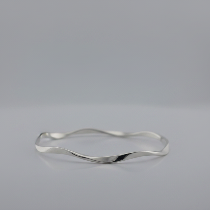 Silver bracelet with a wavy design on a gray background