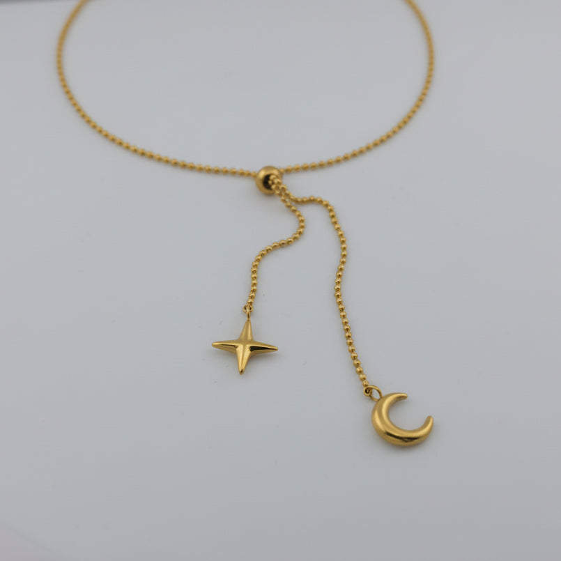 Gold necklace with star and moon pendants on a light gray background