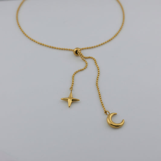 Gold necklace with star and moon pendants on a light gray background