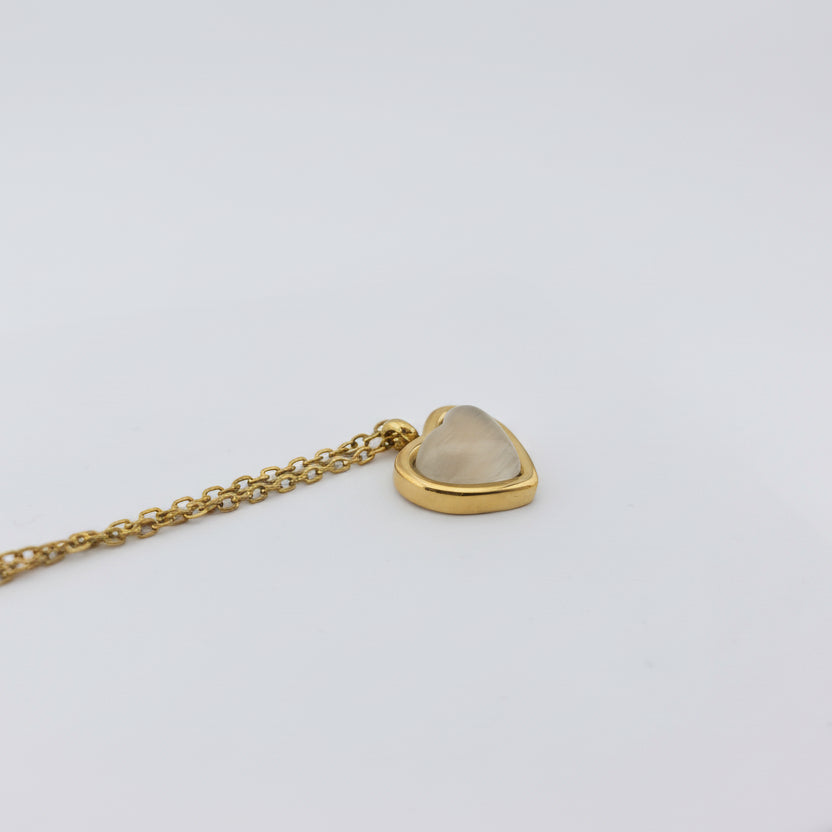 Gold necklace with a heart-shaped pendant on a light gray background