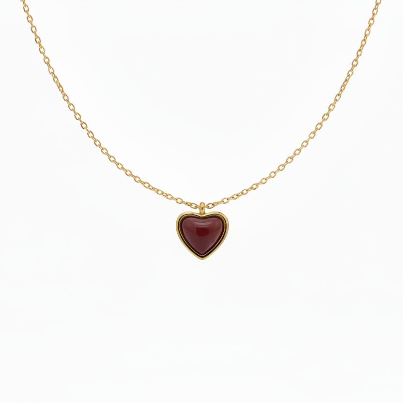 Gold necklace with a heart-shaped red pendant on a light gray background