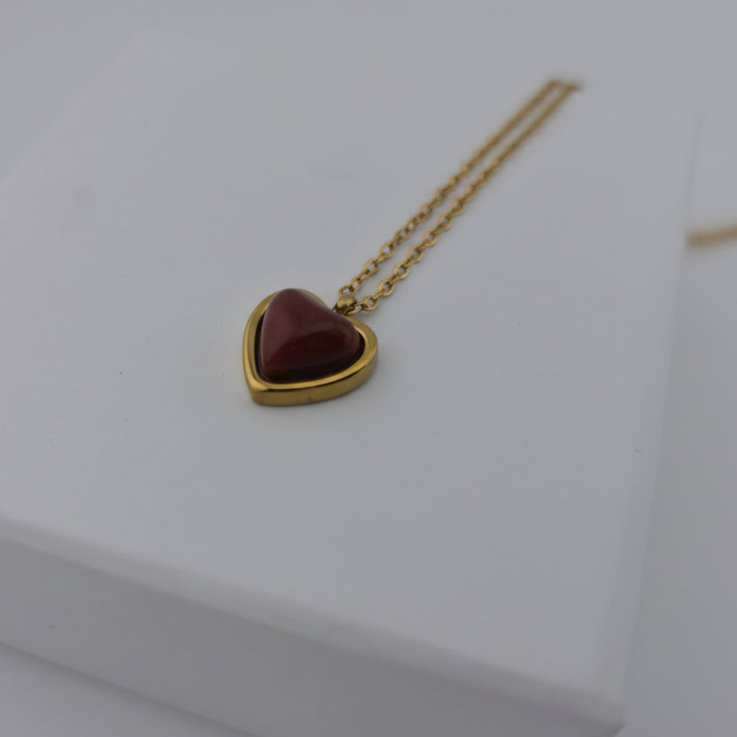 Heart-shaped pendant with gold chain on a white surface