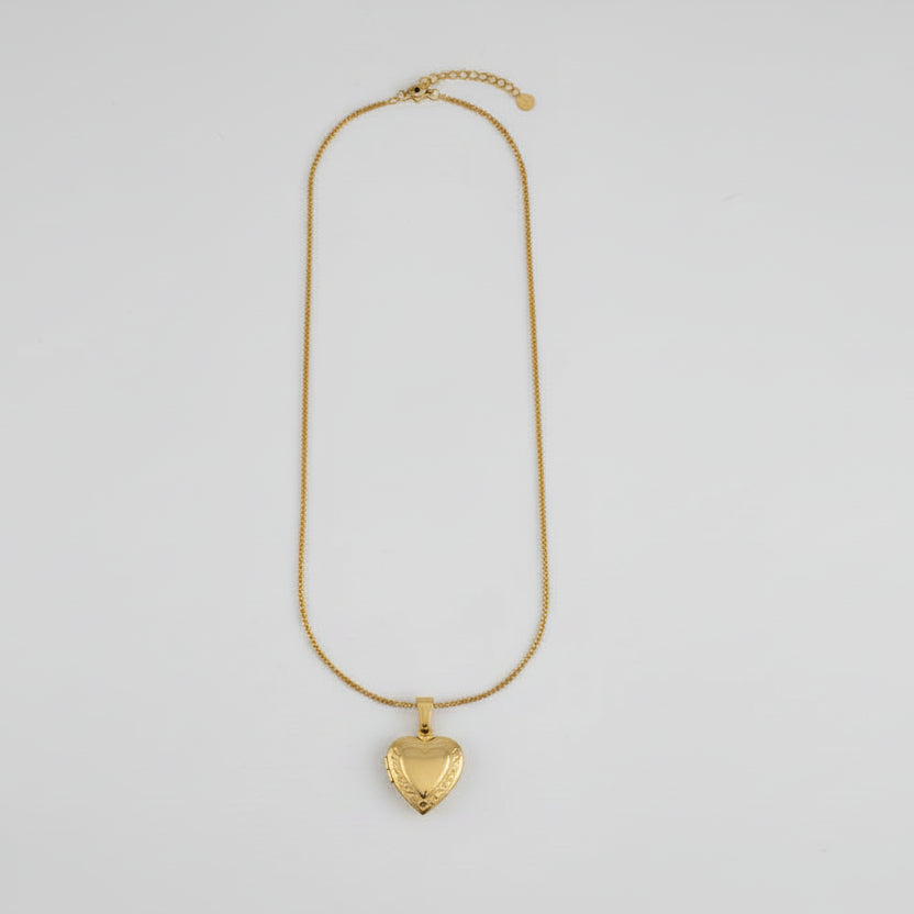 Gold necklace with a heart-shaped pendant on a light gray background