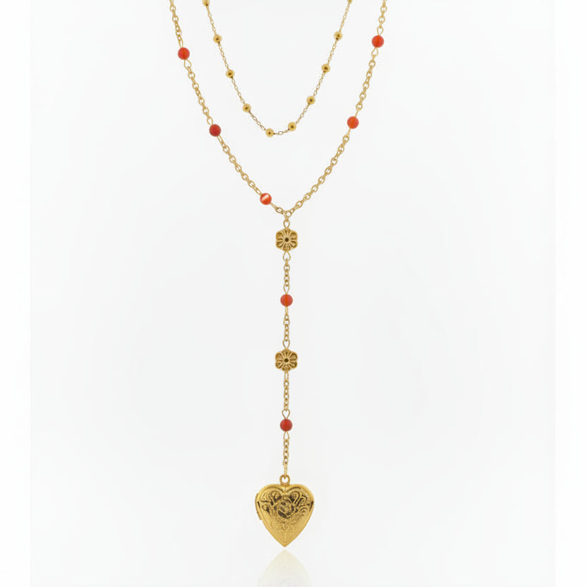 Gold necklace with heart-shaped pendant and red beads on a gray background
