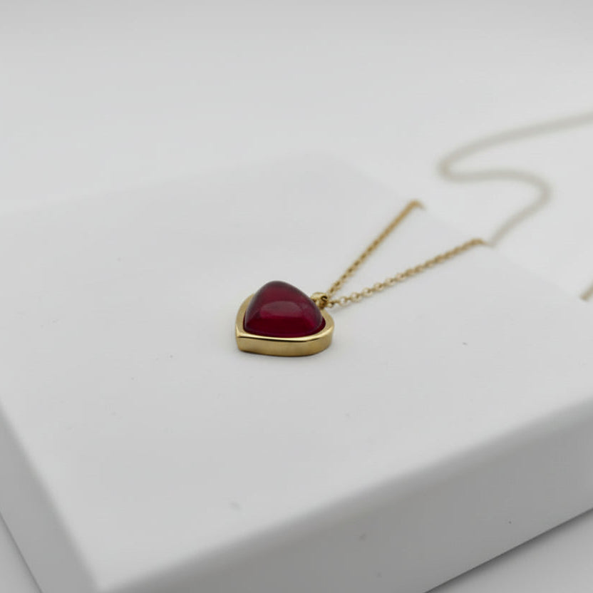 Gold necklace with a heart-shaped red pendant on a white surface