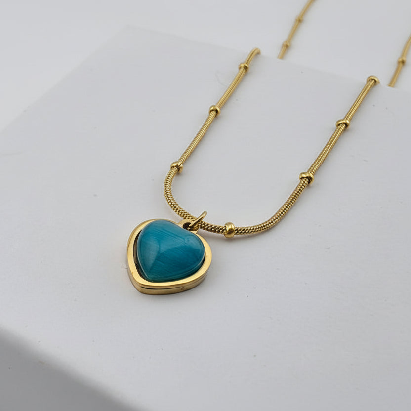 Gold necklace with a turquoise heart pendant on a light gray background