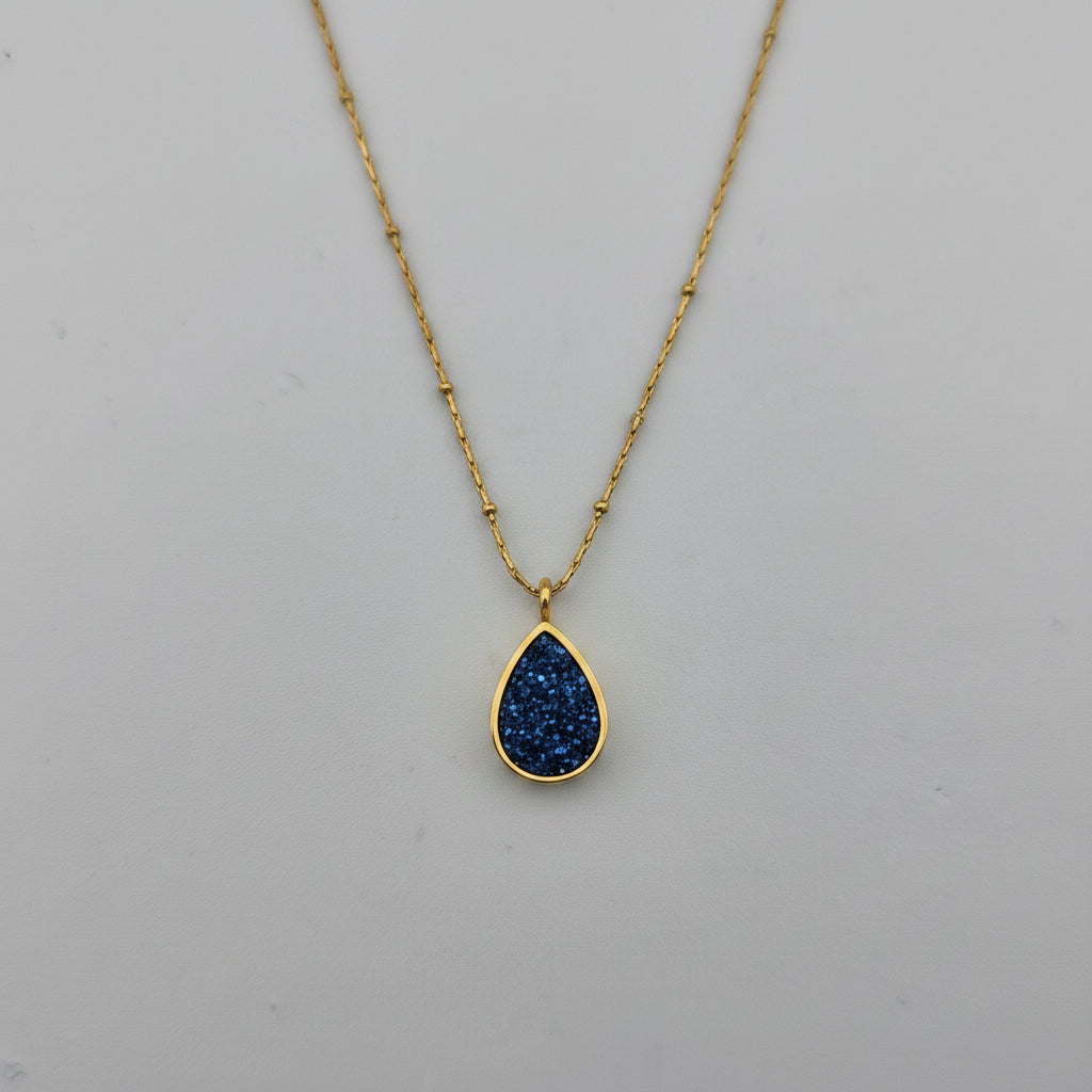 Gold necklace with a blue teardrop pendant on a gray background