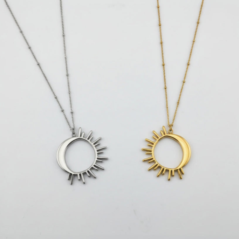 Two sun-shaped necklaces, one silver and one gold, on a light gray background.