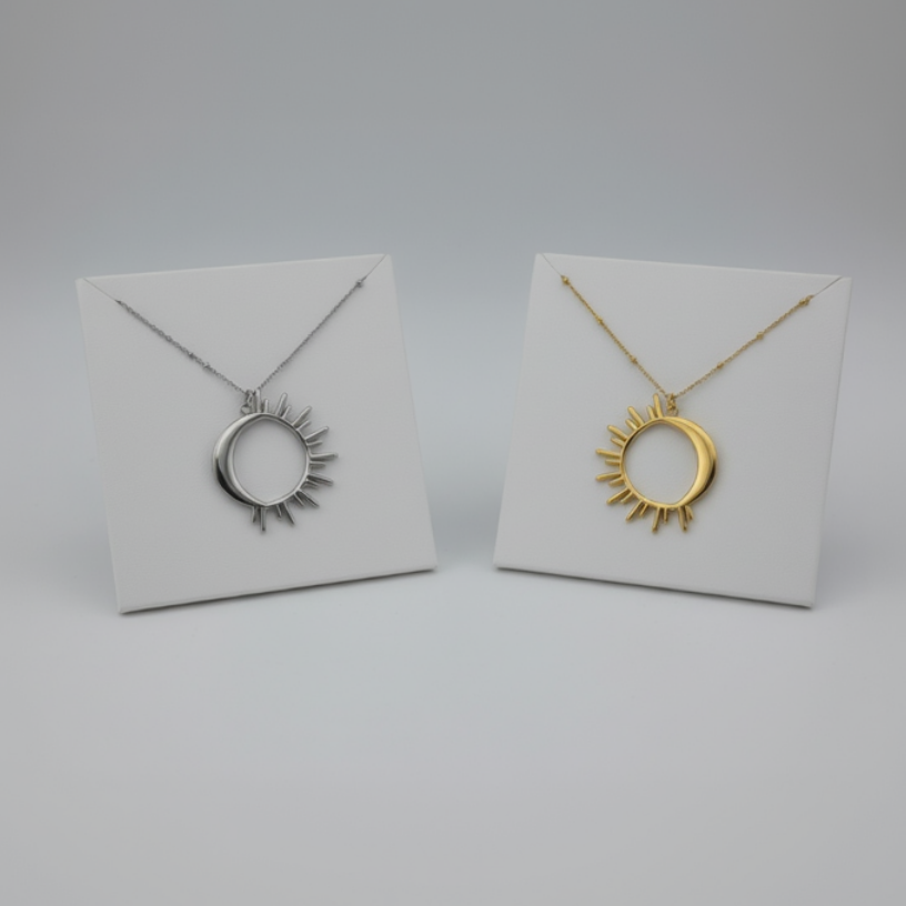Two necklaces with sun design pendants on white display cards against a gray background