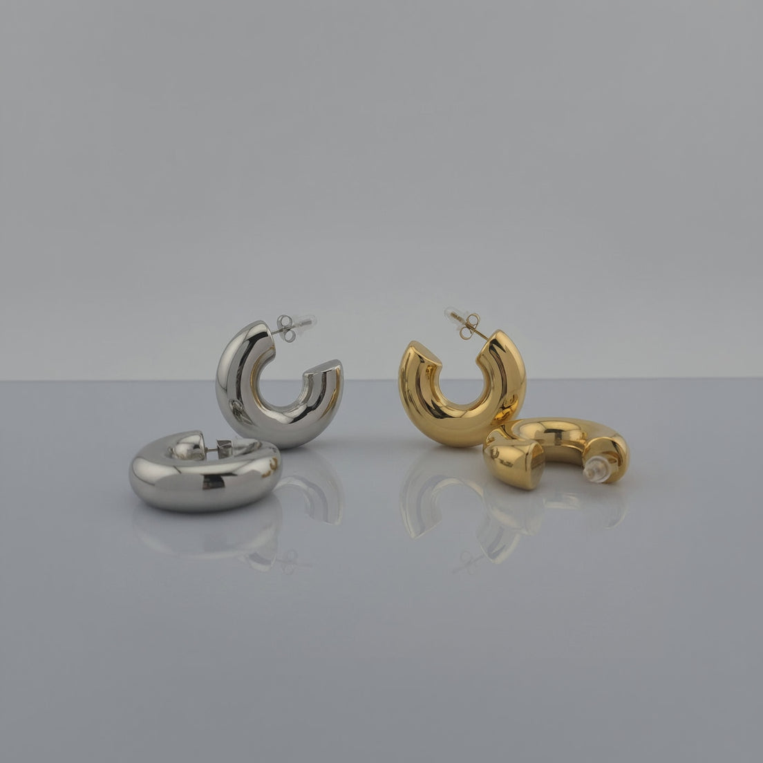 Pair of silver hoop earrings and a pair of gold hoop earrings on a gray background