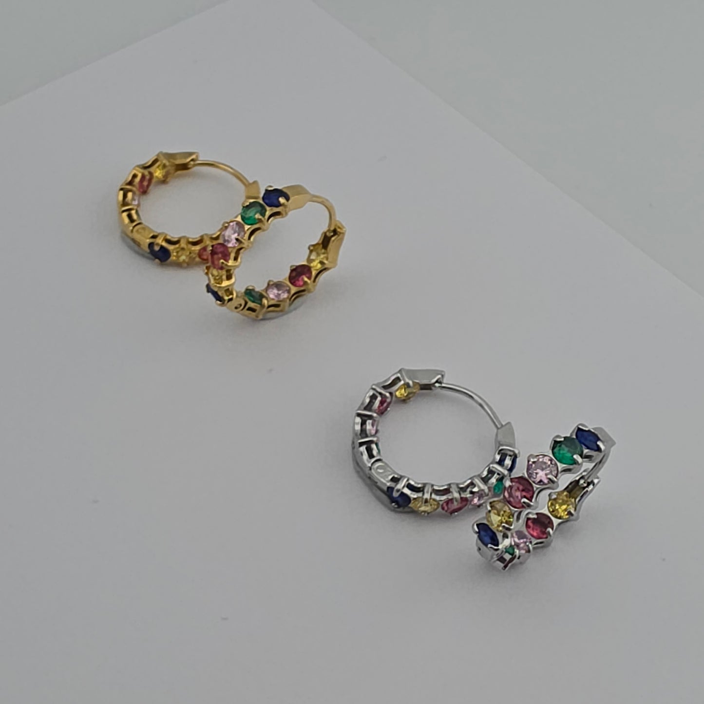 Pair of hoop earrings with colorful gemstones on a light gray background