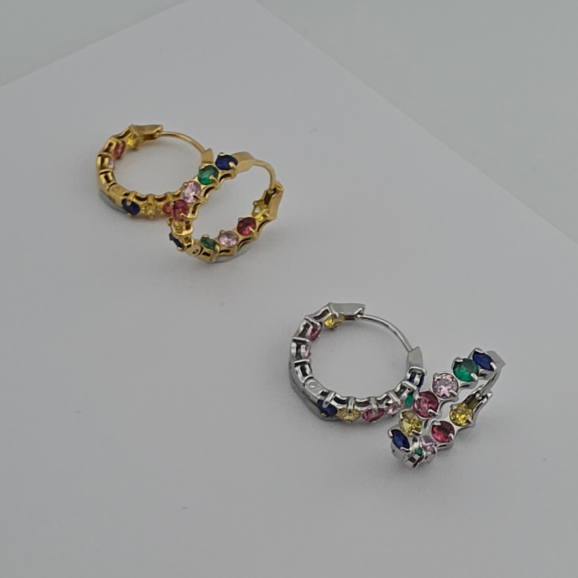 Pair of hoop earrings with colorful gemstones on a light gray background