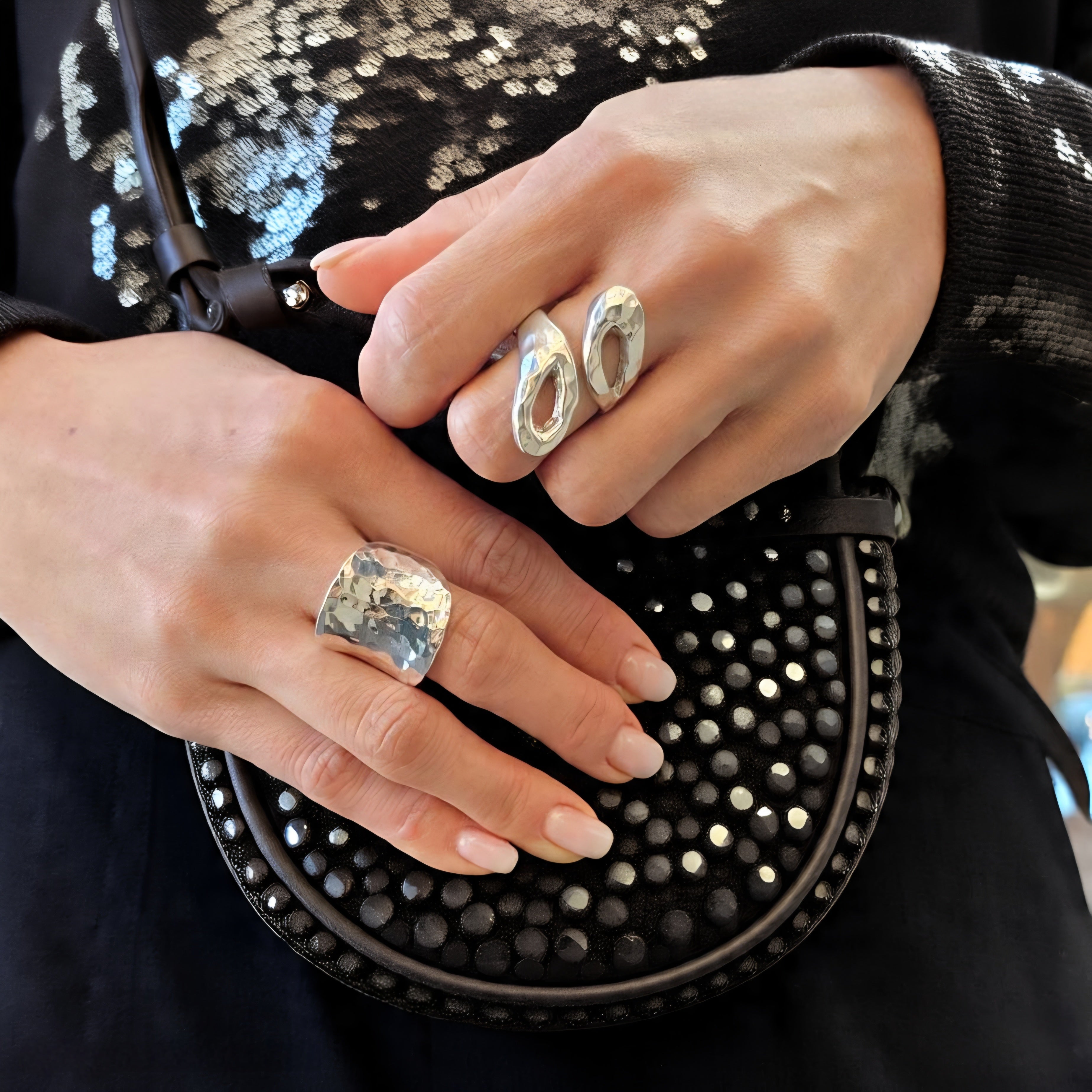Close-up of hands wearing silver rings with a black studded handbag.