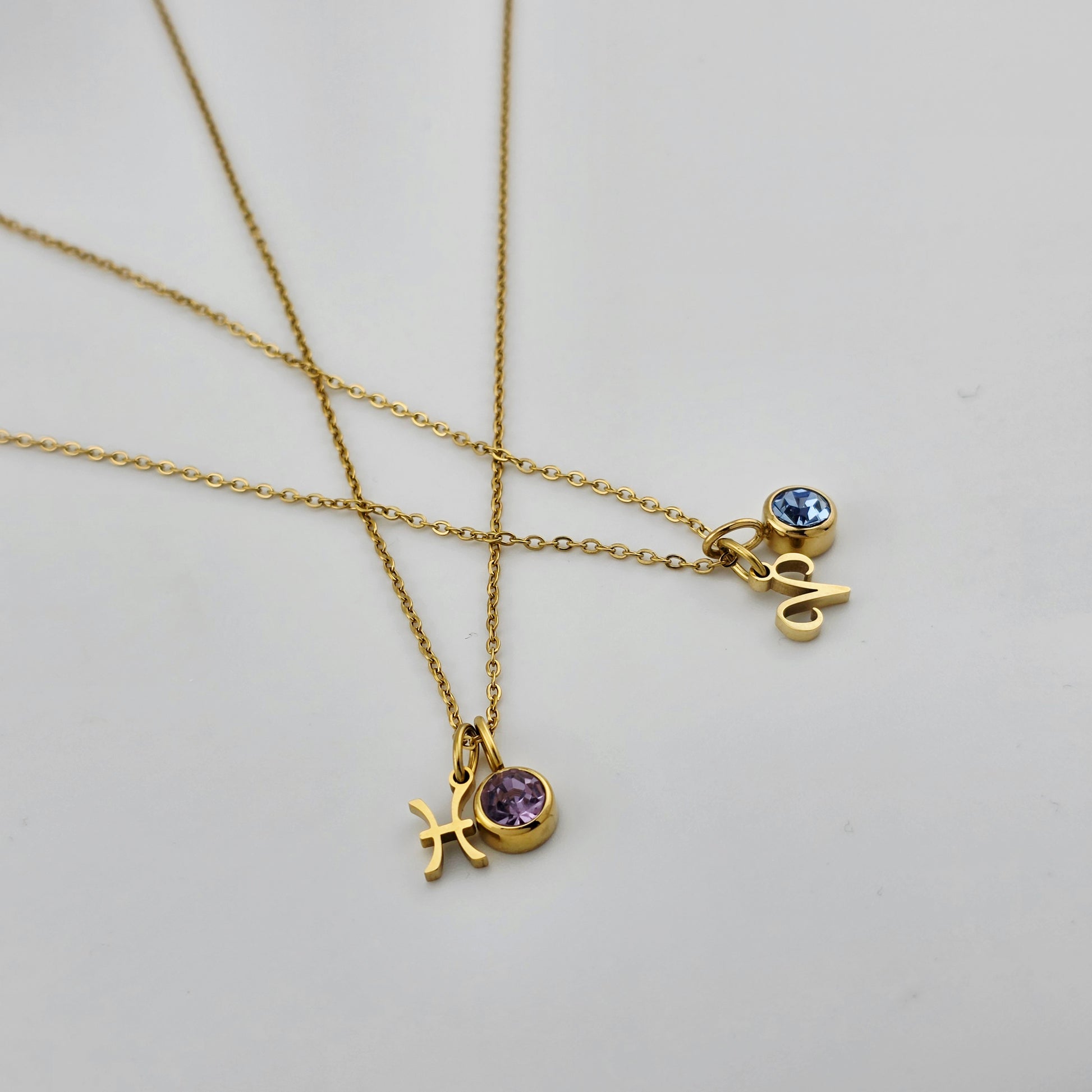 Two gold necklaces with charms on a light gray background