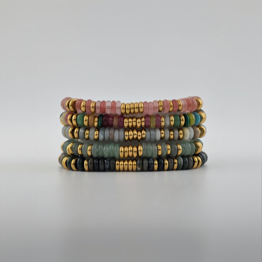 Stack of colorful beaded bracelets with gold accents on a light gray background