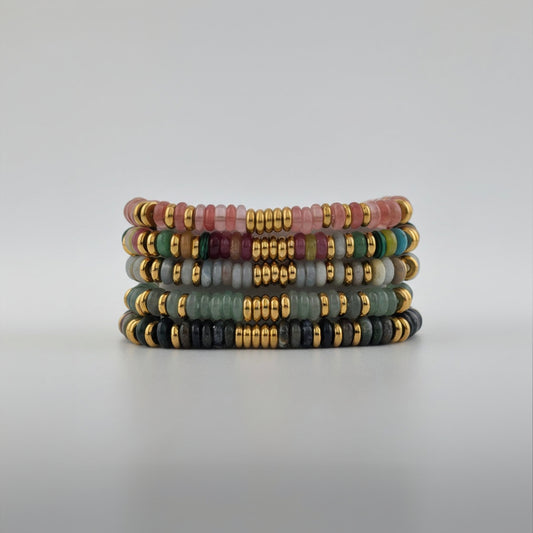 Stack of colorful beaded bracelets with gold accents on a light gray background