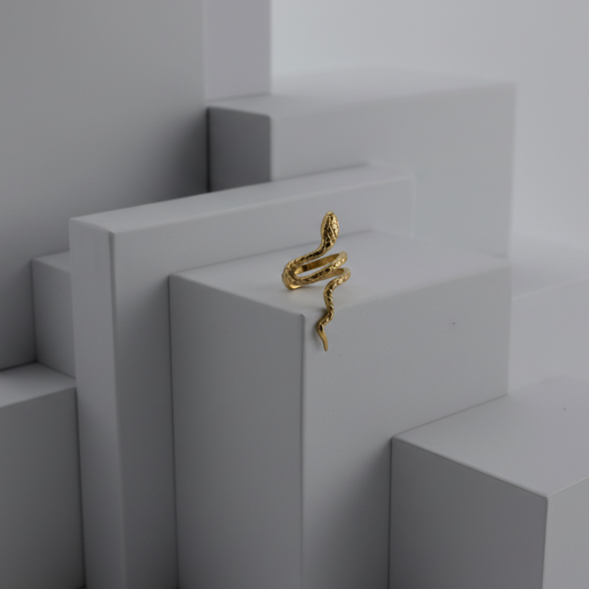 Gold snake-shaped earring on a gray stand with a white background