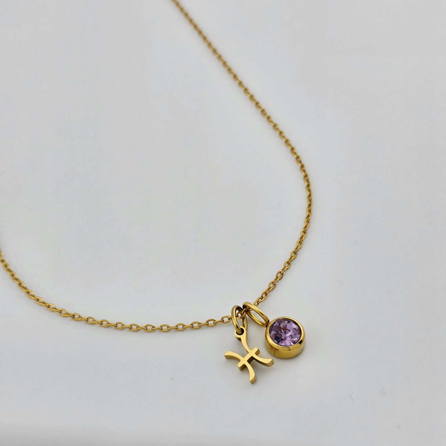 Gold necklace with a purple gemstone and a cross pendant on a light gray background