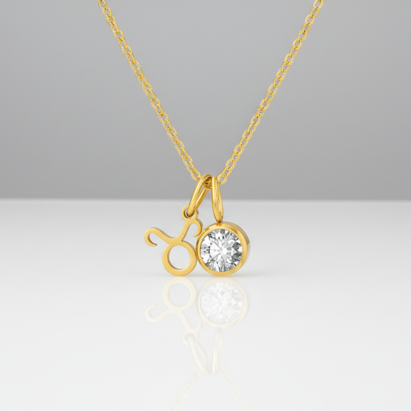 Gold necklace with a zodiac charm and clear gemstone on a white background