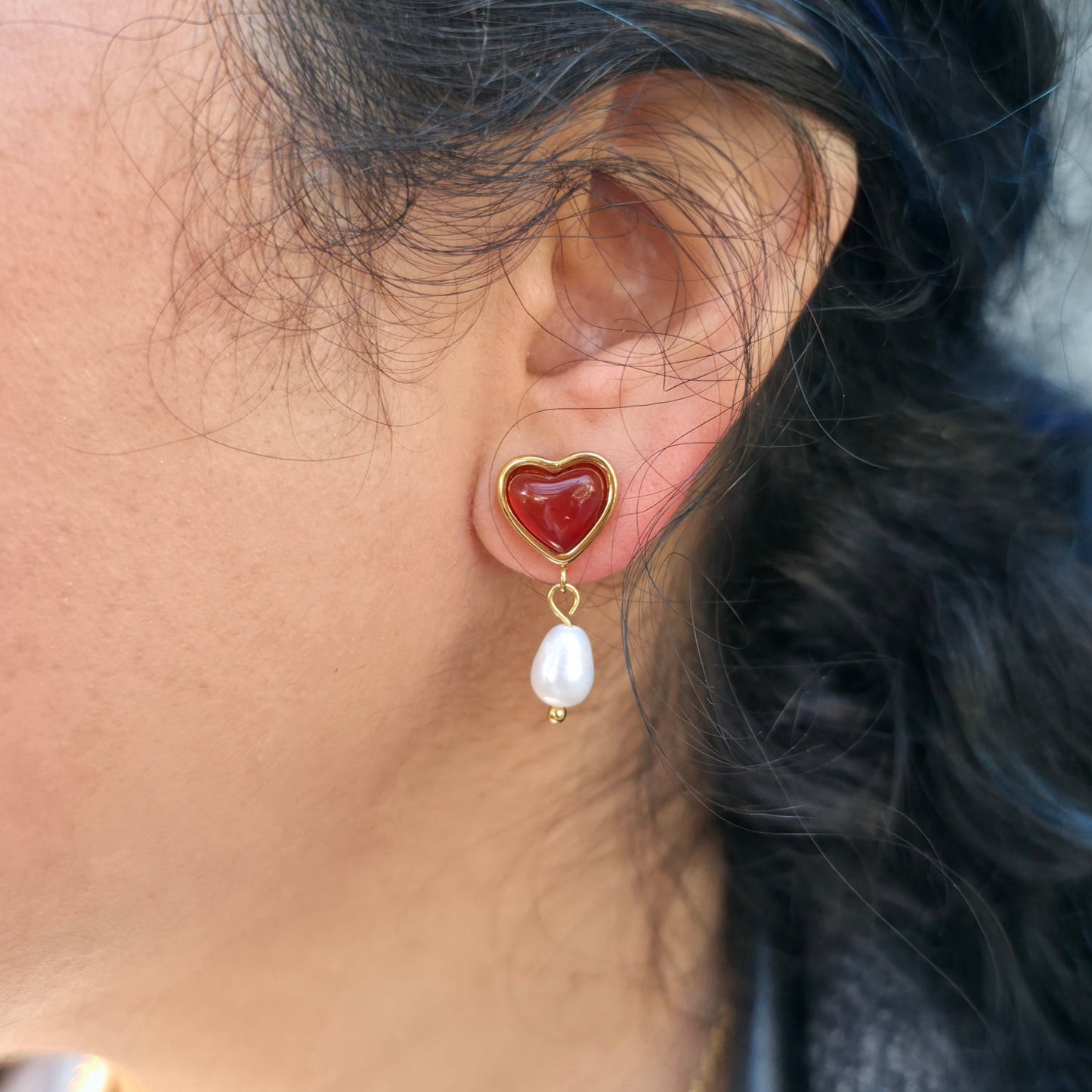 Heart-shaped earring with a pearl drop worn by a person with blue hair.